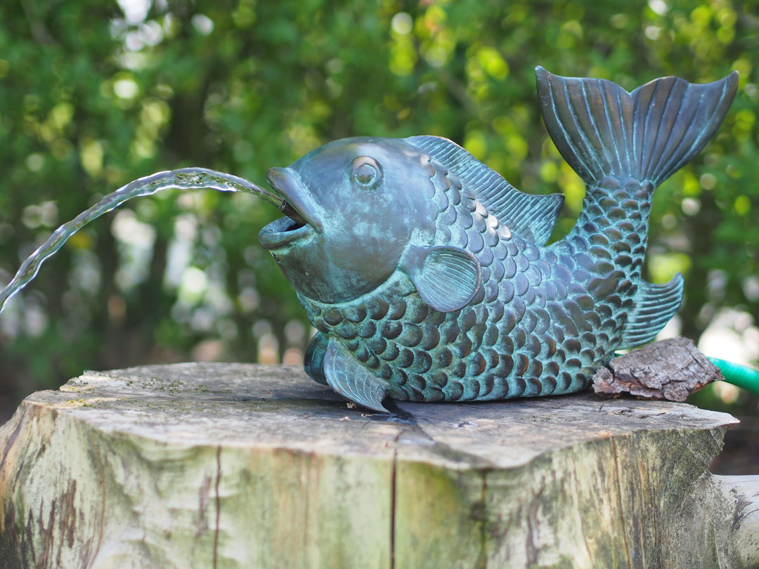 Bronze fish fountain sculpture with joyful design and water flowing from mouth, featuring light-green patina.