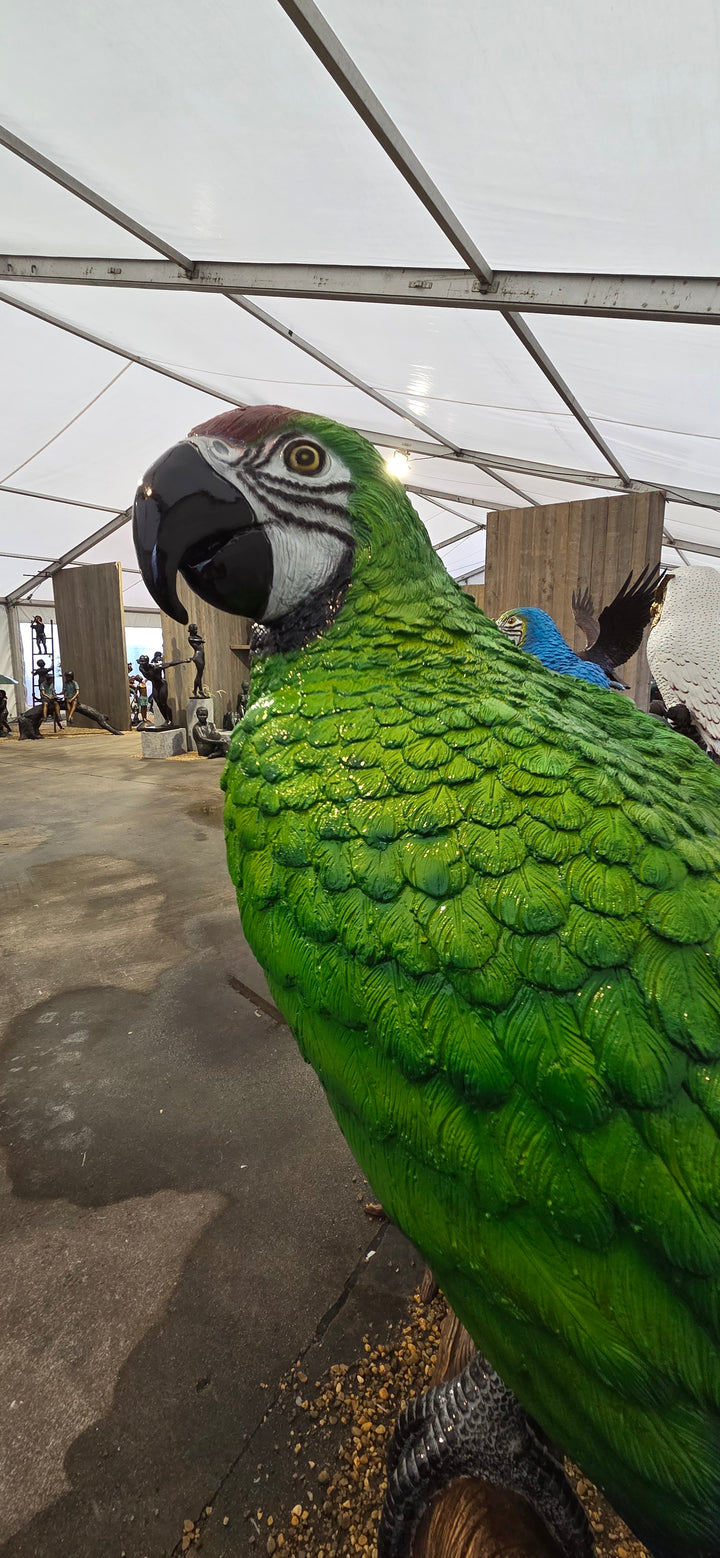 Large bronze sculpture of a green macaw on a tree trunk