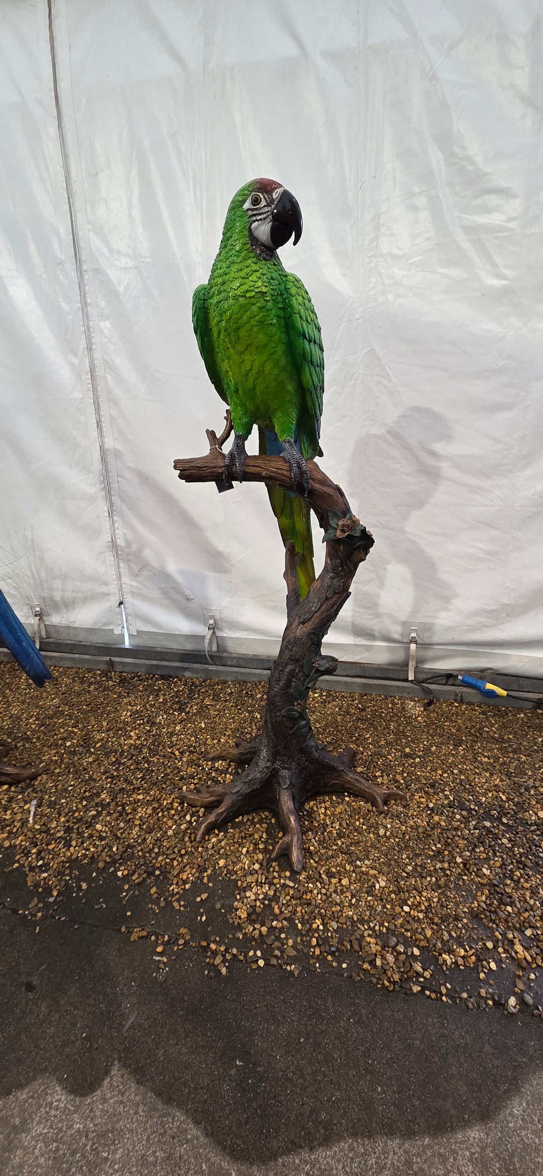 Large bronze sculpture of a green macaw on a tree trunk