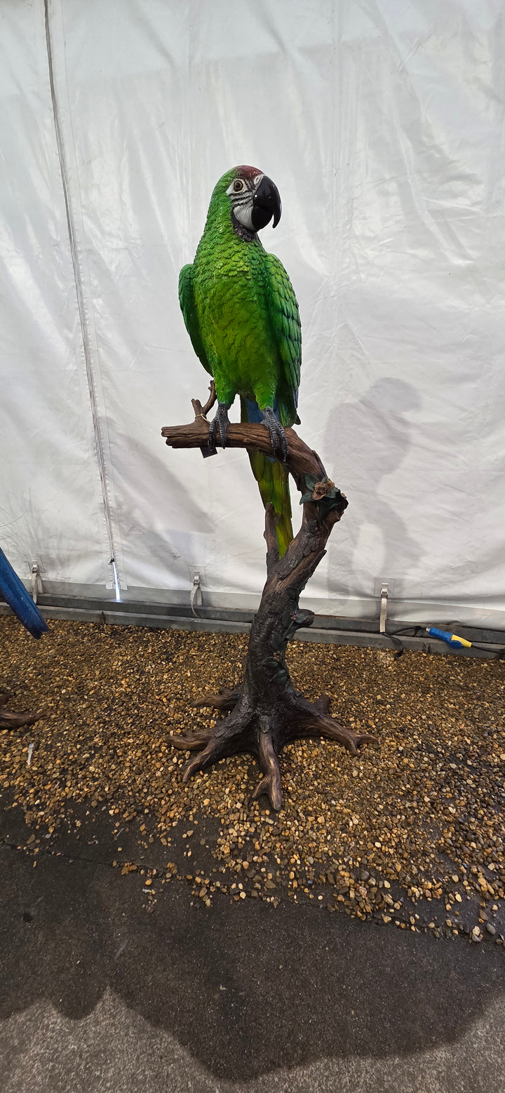 Large bronze sculpture of a green macaw on a tree trunk