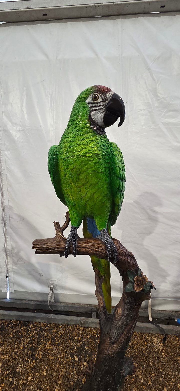 Large bronze sculpture of a green macaw on a tree trunk