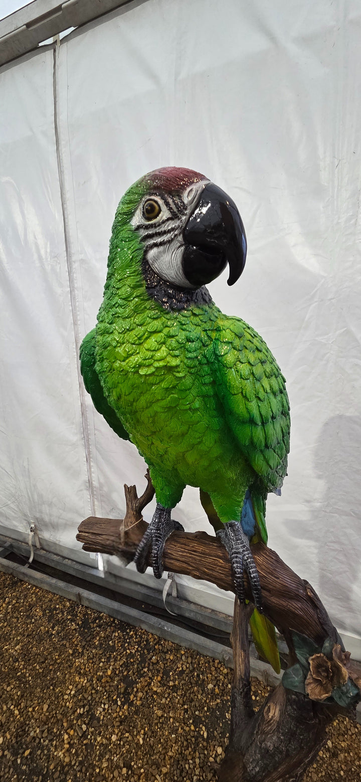Large bronze sculpture of a green macaw on a tree trunk