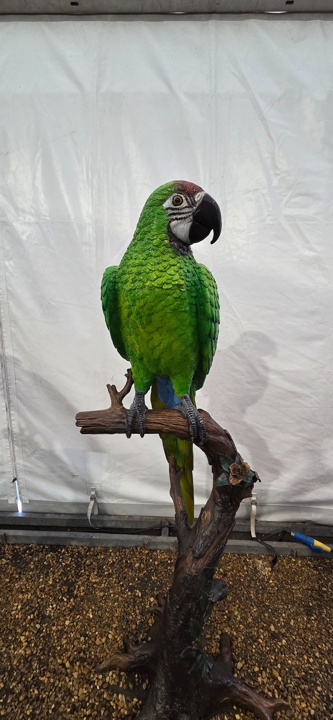 Large bronze sculpture of a green macaw on a tree trunk