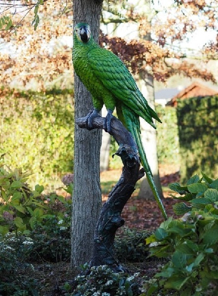 Large bronze sculpture of a green macaw on a tree trunk