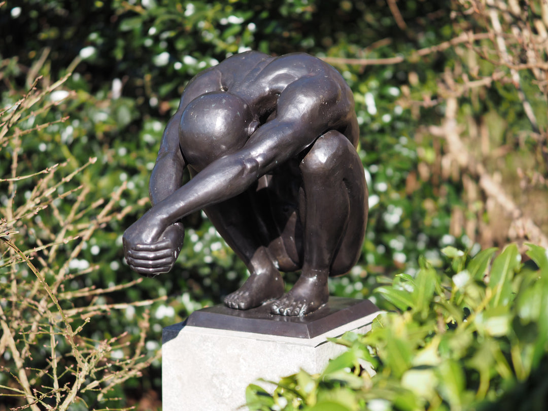 Bronze sculpture of a crouching man in a moment of balance