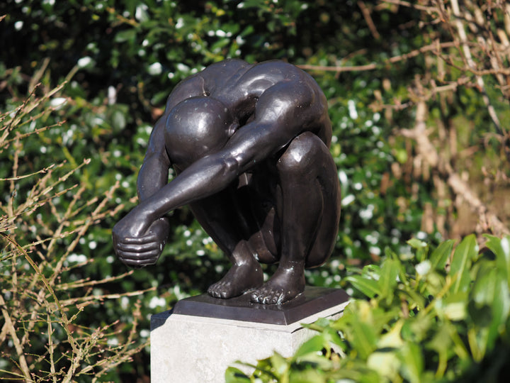 Bronze sculpture of a crouching man in a moment of balance
