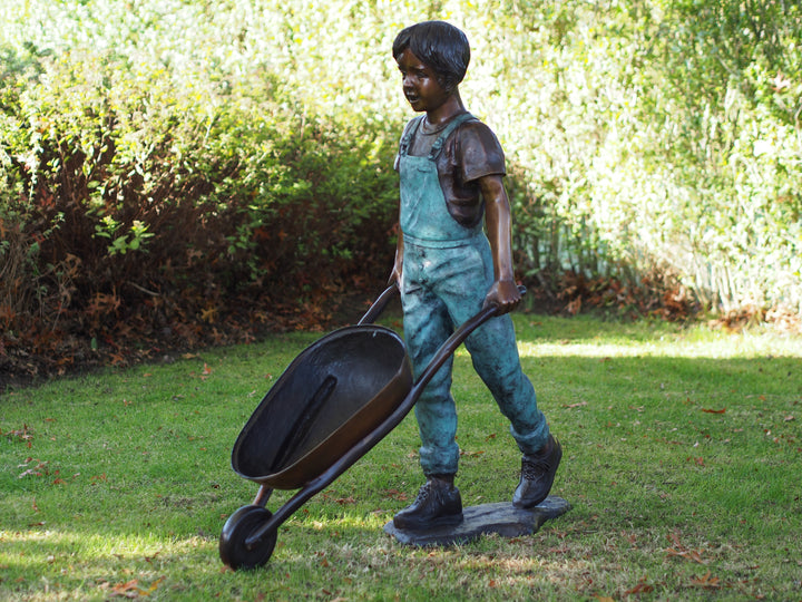 Large bronze sculpture of a young boy with a wheelbarrow