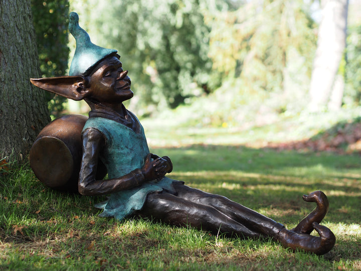Bronze sculpture of a pixie sitting against a barrel