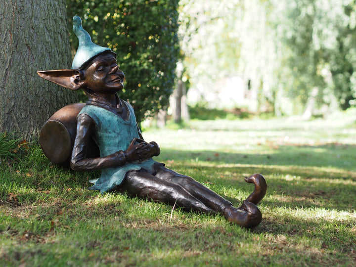 Bronze sculpture of a pixie sitting against a barrel