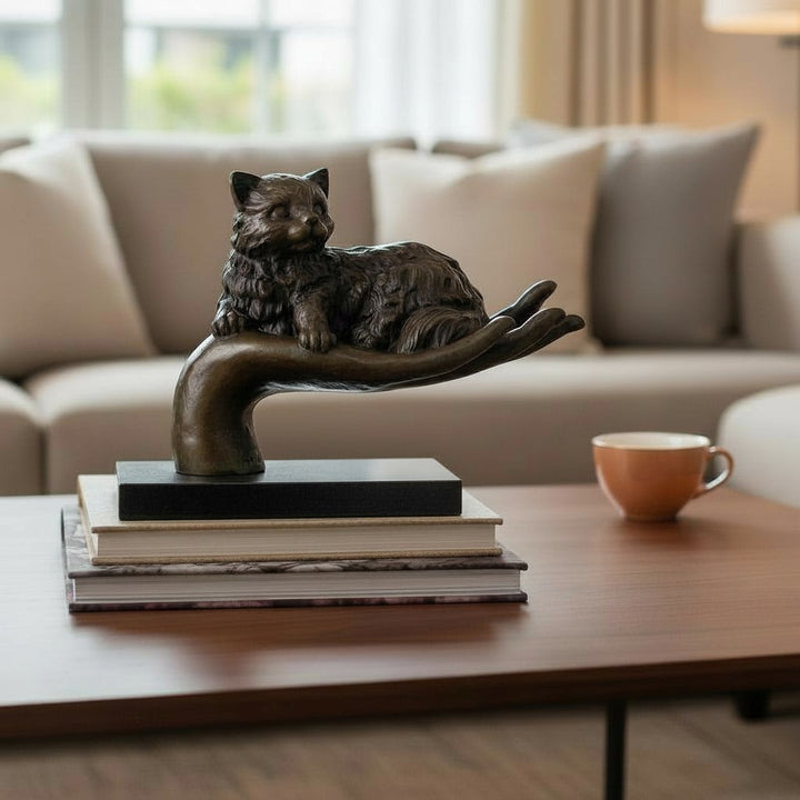 Escultura de bronce de un gato descansando en una mano