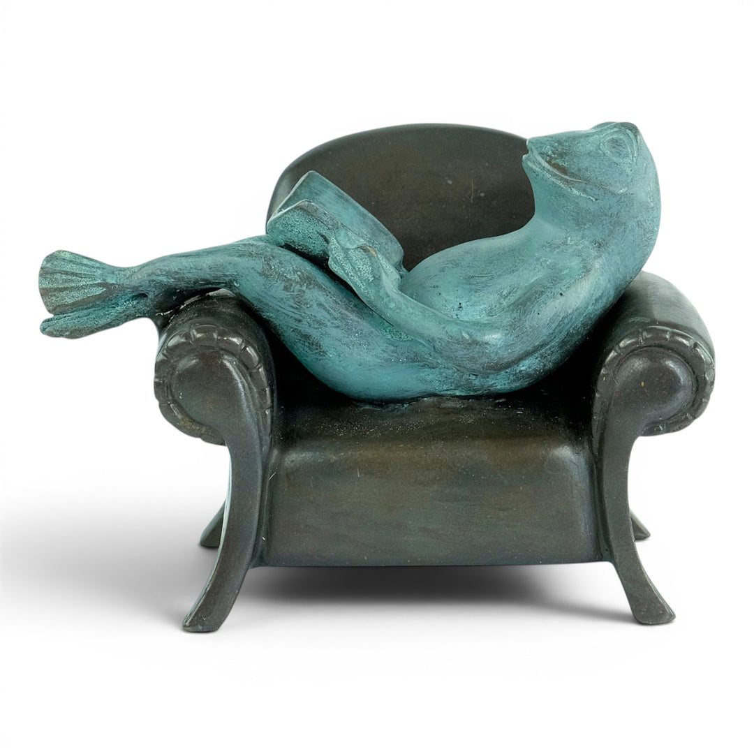 Escultura de bronce de una rana leyendo en un sillón