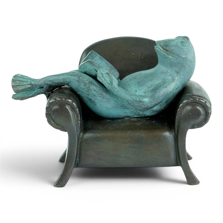 Escultura de bronce de una rana leyendo en un sillón
