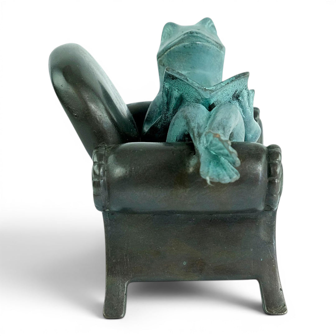Escultura de bronce de una rana leyendo en un sillón