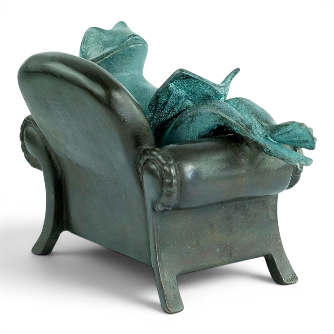 Escultura de bronce de una rana leyendo en un sillón