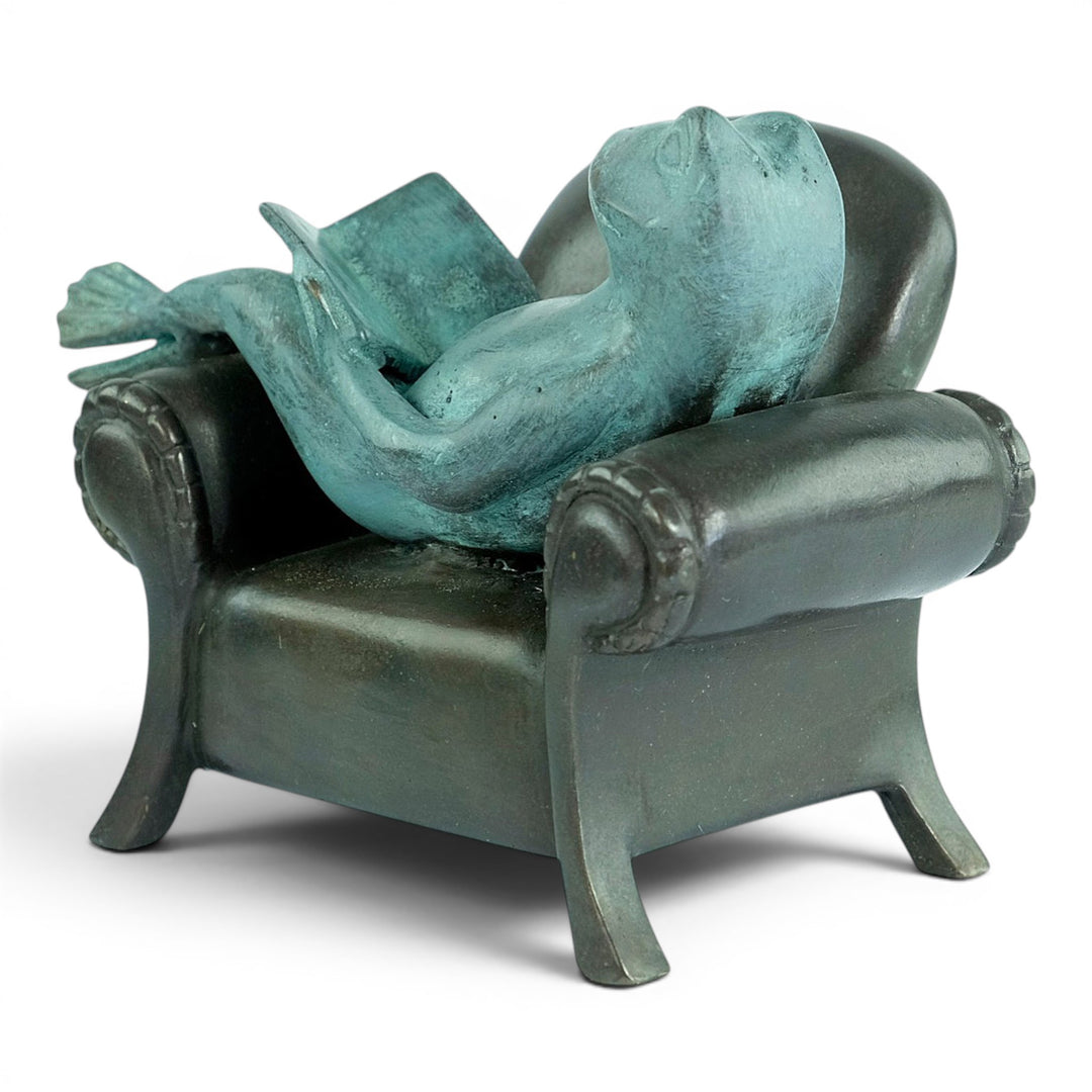 Escultura de bronce de una rana leyendo en un sillón
