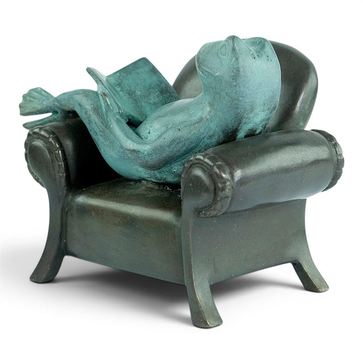 Escultura de bronce de una rana leyendo en un sillón