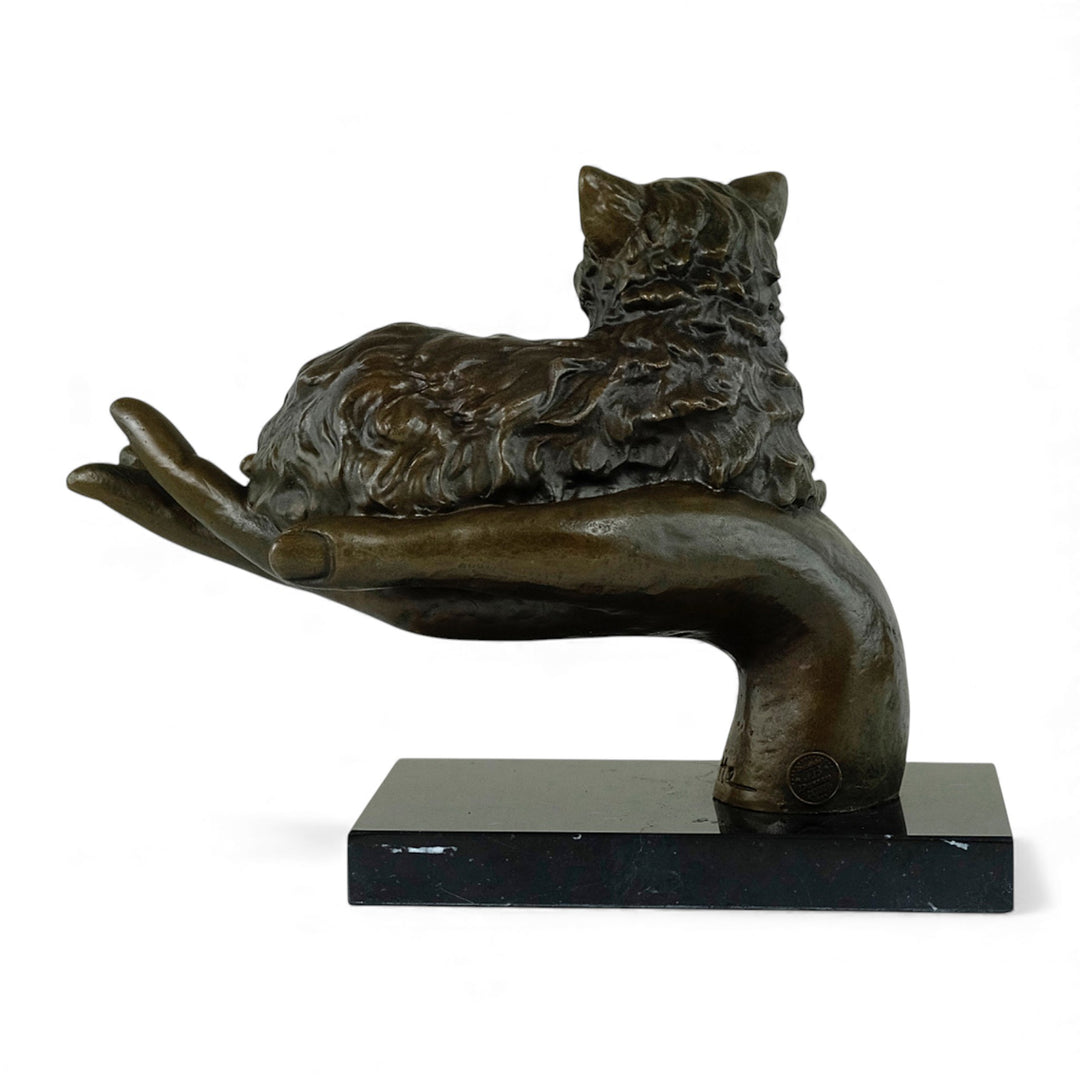 Escultura de bronce de un gato descansando en una mano
