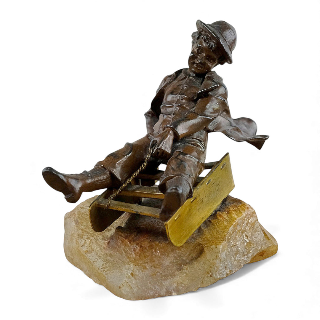 Escultura antigua de bronce de un niño en un trineo.