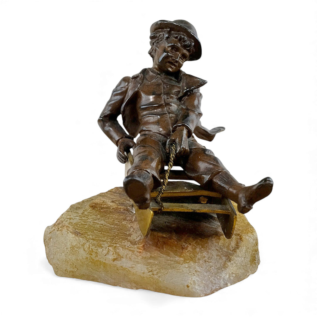 Escultura antigua de bronce de un niño en un trineo.