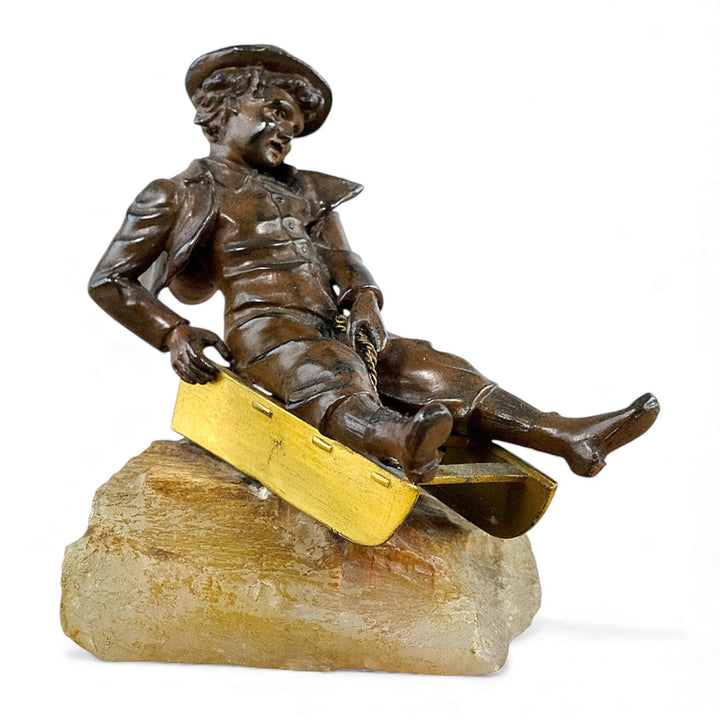 Escultura antigua de bronce de un niño en un trineo.