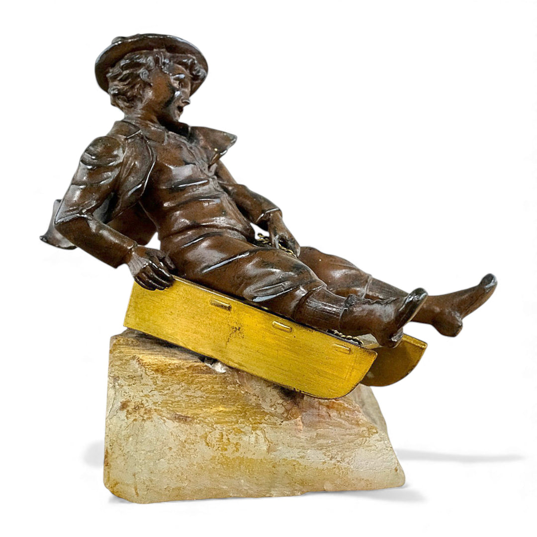 Escultura antigua de bronce de un niño en un trineo.