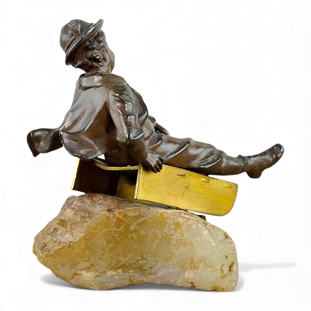 Escultura antigua de bronce de un niño en un trineo.