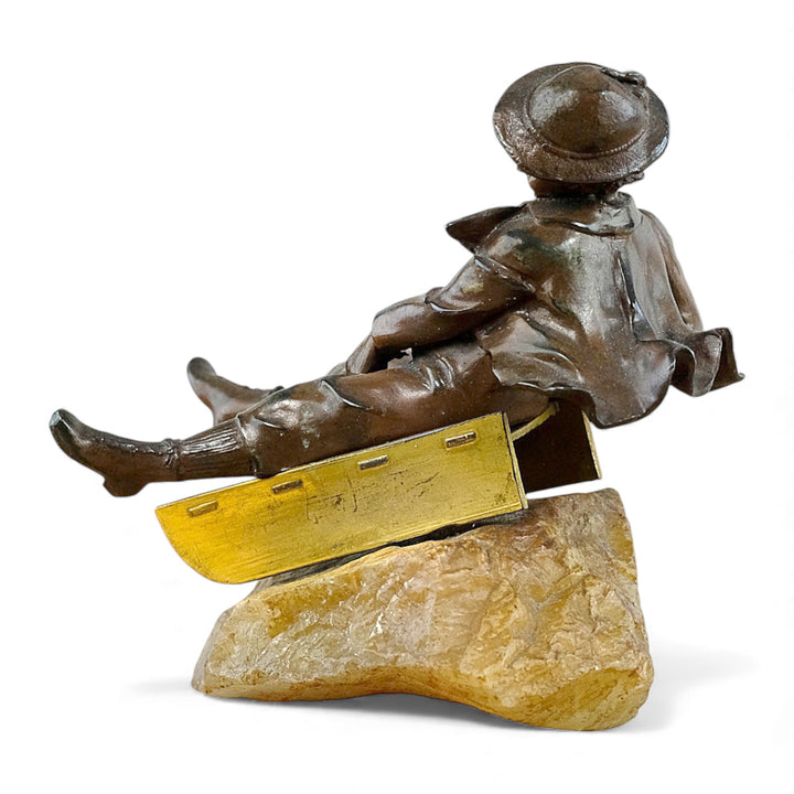 Escultura antigua de bronce de un niño en un trineo.