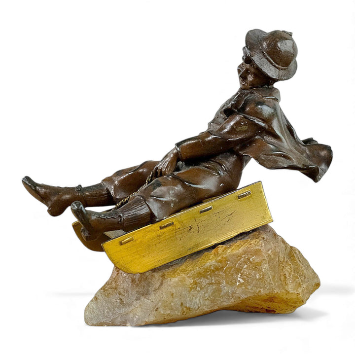 Escultura antigua de bronce de un niño en un trineo.