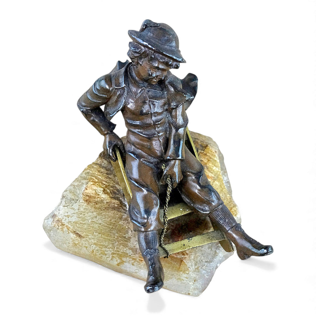 Escultura antigua de bronce de un niño en un trineo.