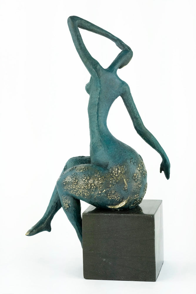 Modern bronze sculpture of a female sitting in a graceful pose