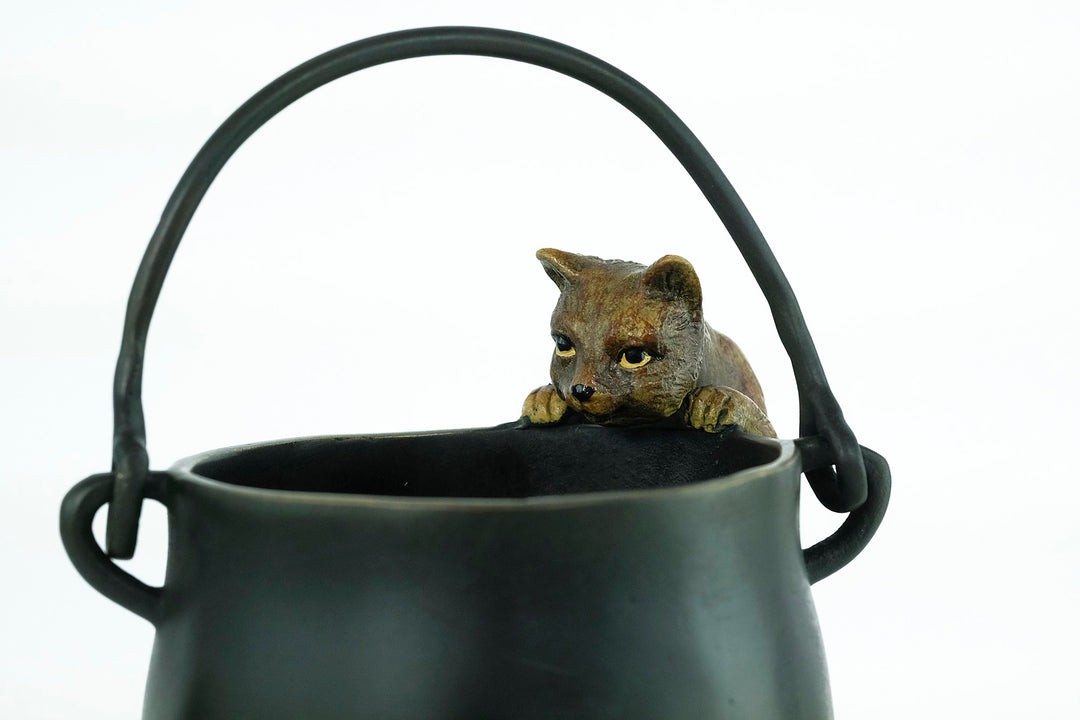 Bronze sculpture of a curious cat climbing into a cauldron