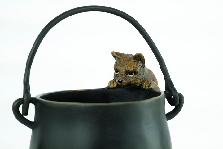 Bronze sculpture of a curious cat climbing into a cauldron