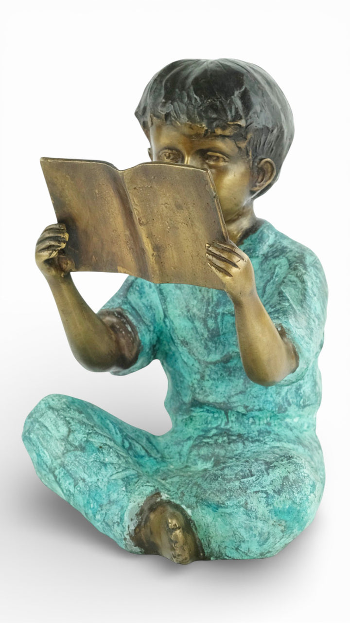 Escultura de bronce de un joven sentado leyendo un libro