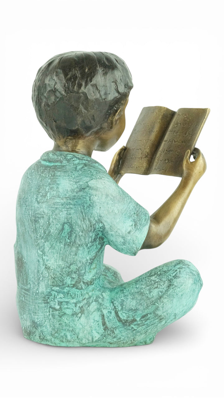 Escultura de bronce de un joven sentado leyendo un libro
