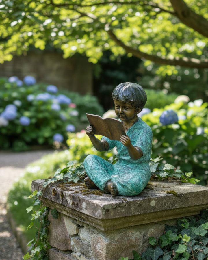 Escultura de bronce de un joven sentado leyendo un libro