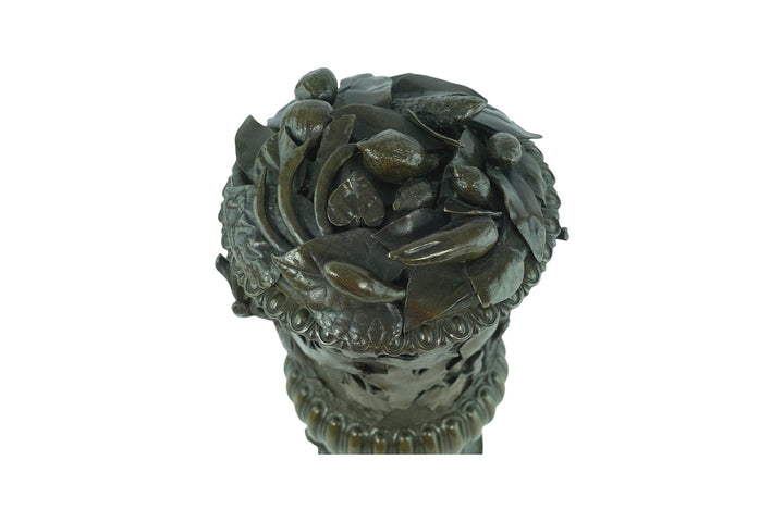 Close-up of antique bronze vase top with detailed oak leaves and fruit decorations, showcasing intricate craftsmanship.