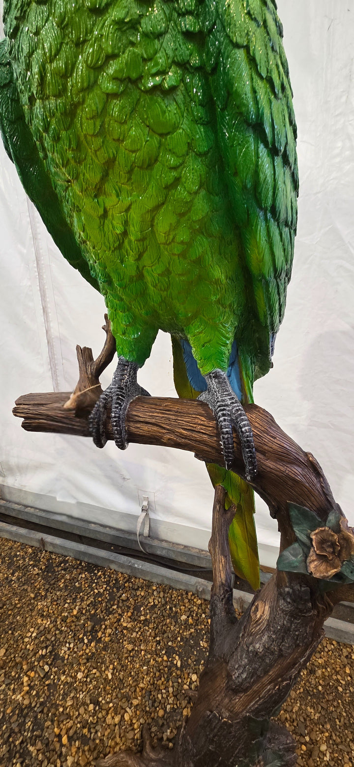 Large bronze sculpture of a green macaw on a tree trunk