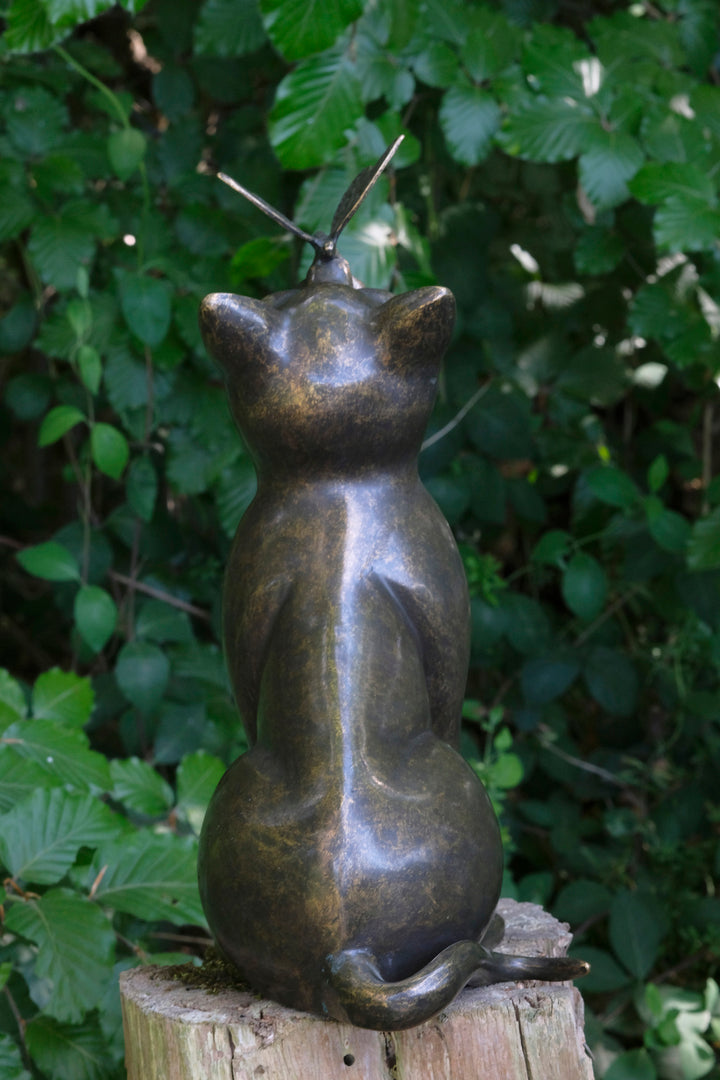 Bronze sculpture of a cat with a butterfly on its nose, showcasing playful elegance and charm in a garden setting.