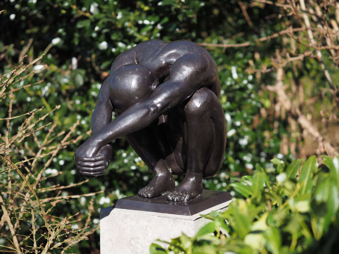 Bronze crouching man sculpture in balance, featuring dark patina, ideal for indoor or outdoor display.