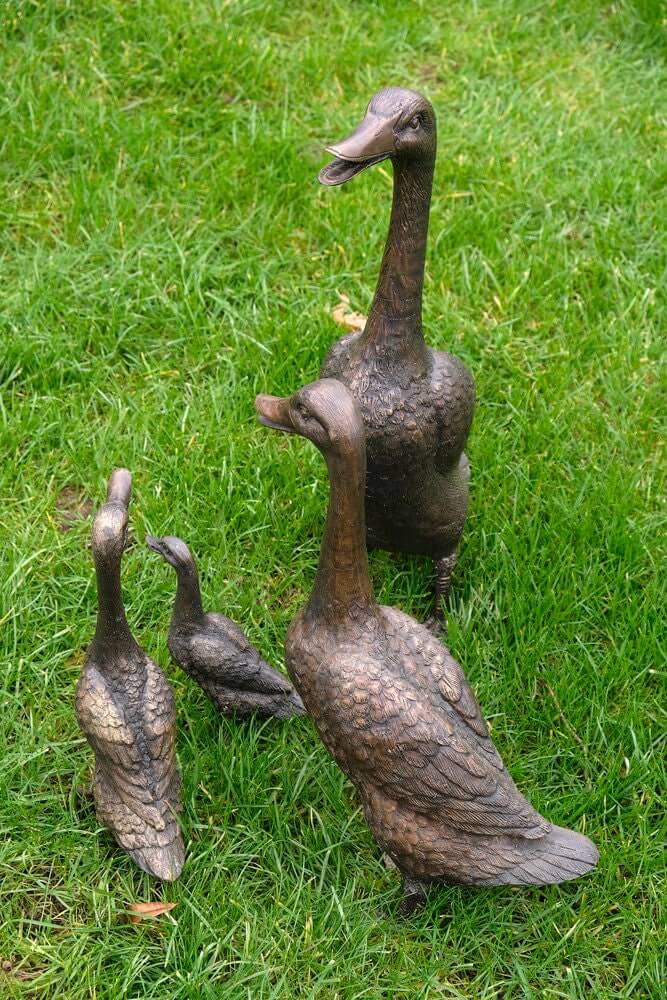 Set of 4 bronze duck sculptures including mother, father, and two ducklings on grass for outdoor decoration.