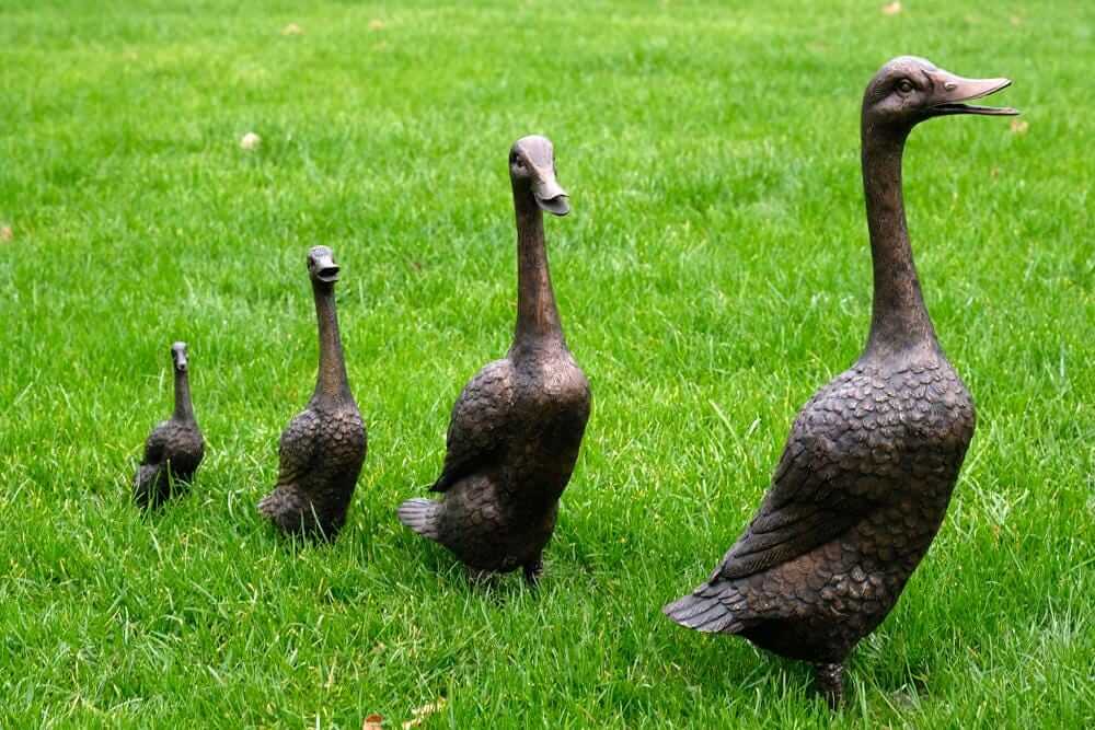 Set of 4 bronze duck family sculptures on green grass, perfect for outdoor or indoor decoration.