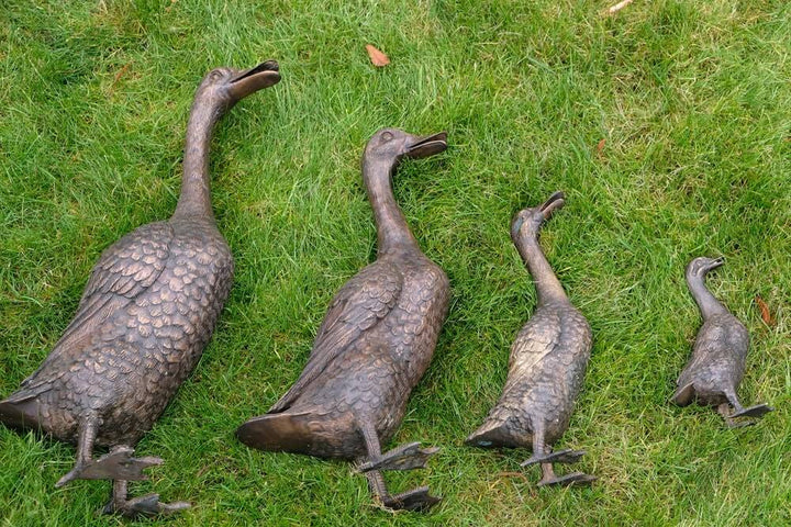 Set of 4 bronze duck family sculptures on grass, featuring mother, father, and two ducklings for outdoor decoration.