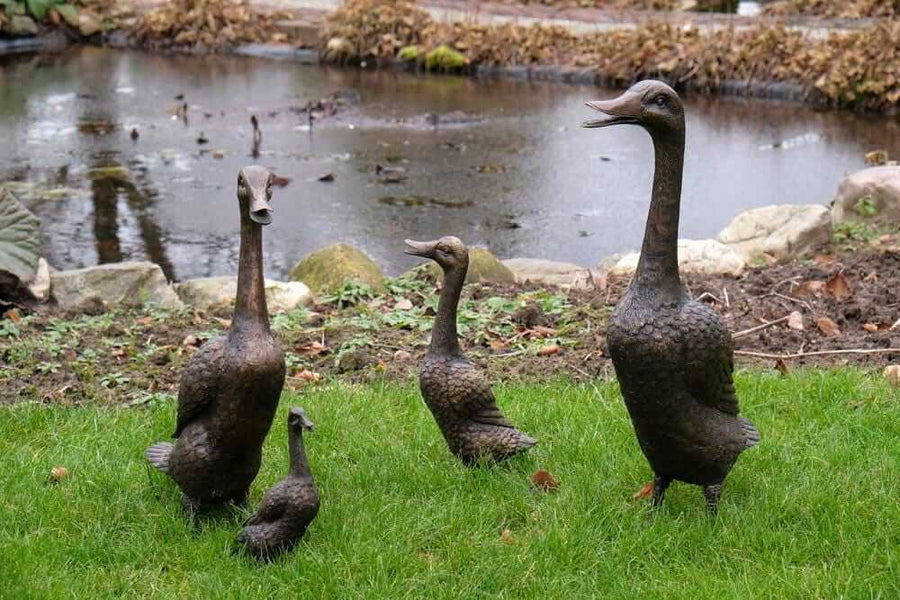 Set of 4 bronze duck family sculptures in garden near pond, perfect for outdoor decoration and display.