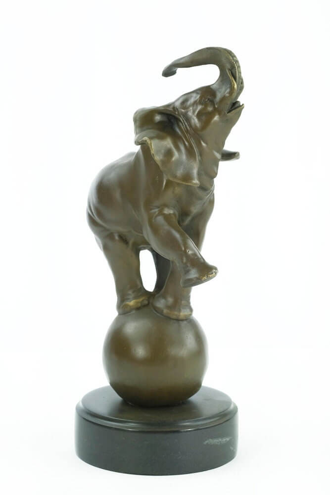 Bronze elephant sculpture balancing on a ball with a round marble base, playful decorative art piece.