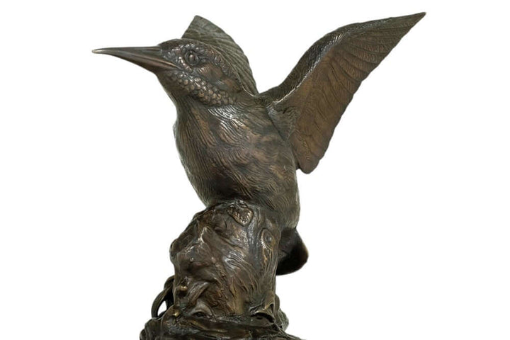 Bronze sculpture of a king fisher with wings spread, intricately detailed, on a decorative tree trunk.