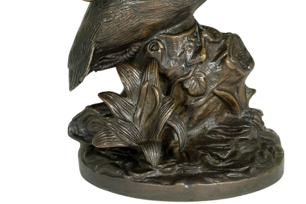 Close-up of a detailed bronze king fisher sculpture with floral decor on a tree trunk, showcasing intricate details.