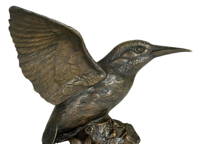 Bronze sculpture of a kingfisher with spread wings on a tree trunk, detailed with floral accents.