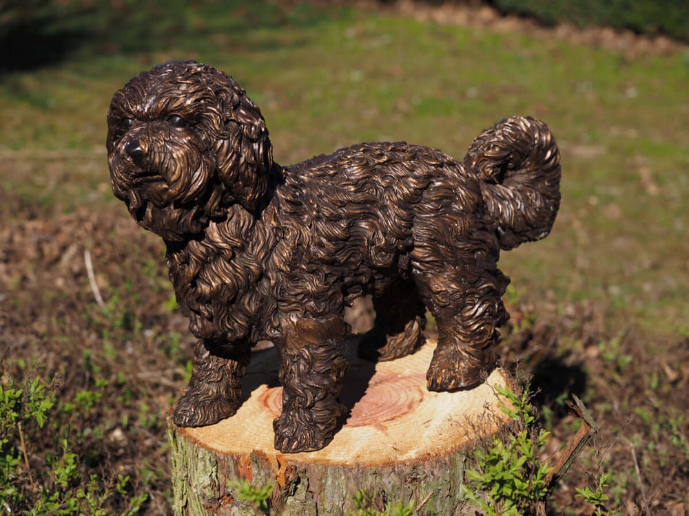 Bronze labradoodle sculpture in fine detail on a wooden stump, showcasing curly coat and playful spirit.