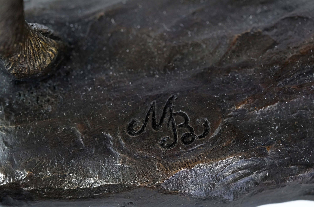 Close-up of the signature 'MB' on the base of a bronze moose sculpture, showcasing the artist's detail.