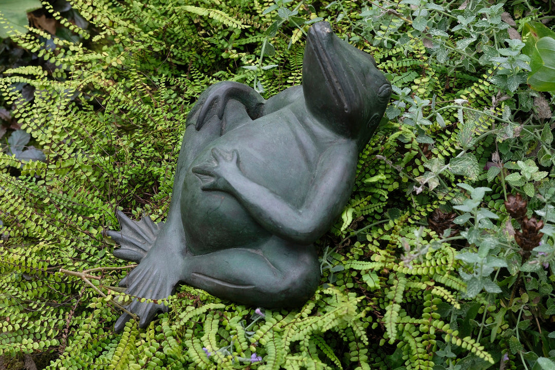 Bronze sculpture of a relaxing frog with green patina among ferns, perfect for indoor and outdoor decor.